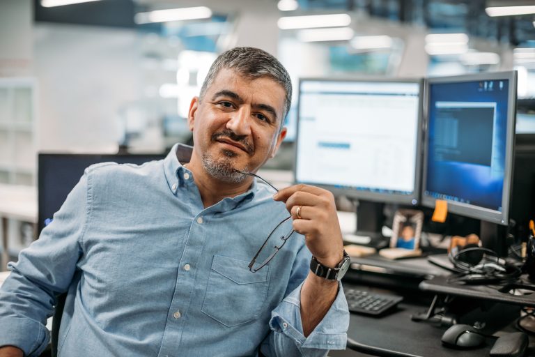 Asian Middle Eastern businessman sitting in office with eyeglasses and computer terminal